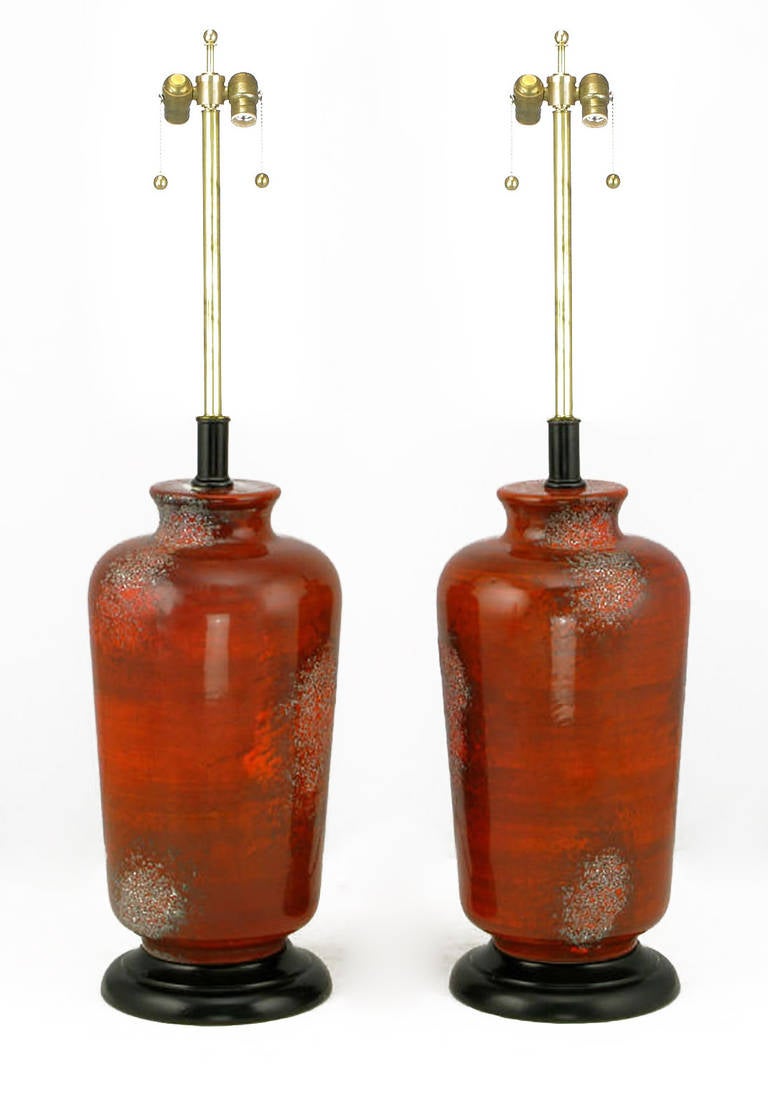 Unique table lamps look as though they were formed from molten lava. Deep textured red glaze over vermillion ceramic vase form bodies. The bases and stems are black lacquered wood and metal, respectively. Sold sans shades.