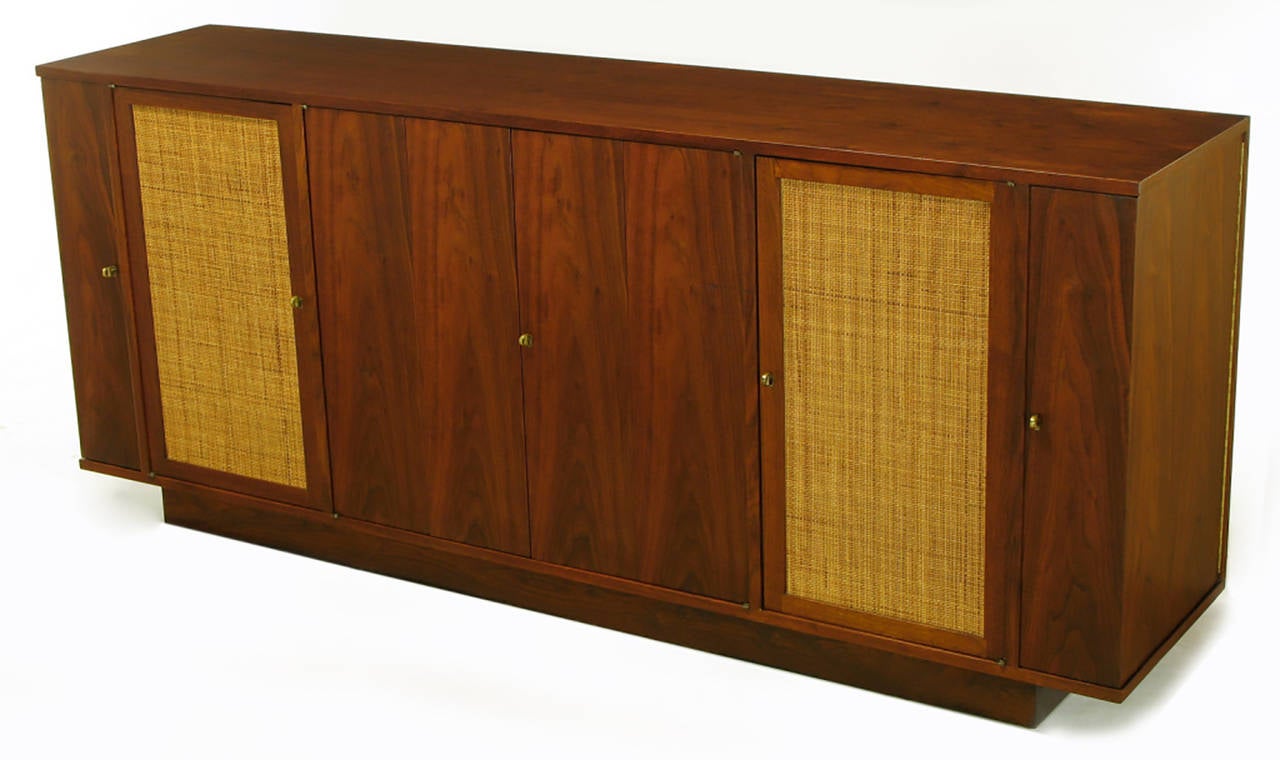 Edward Wormley for Dunbar walnut and cane sideboard on recessed plinth base. Gullwing style side doors open to reveal three storage compartments for each door. Centre figured walnut doors open to compartment with single drawer and shelf. Cane front