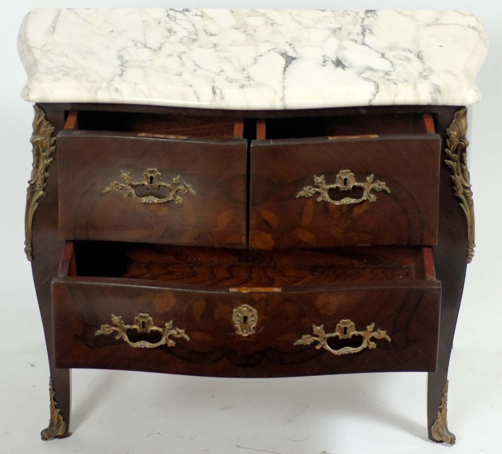 Elegant darker finished pair of twentieth century marble-topped bombe commodes with subtle floral marquetry of mixed veneers, and bronze mounts.
