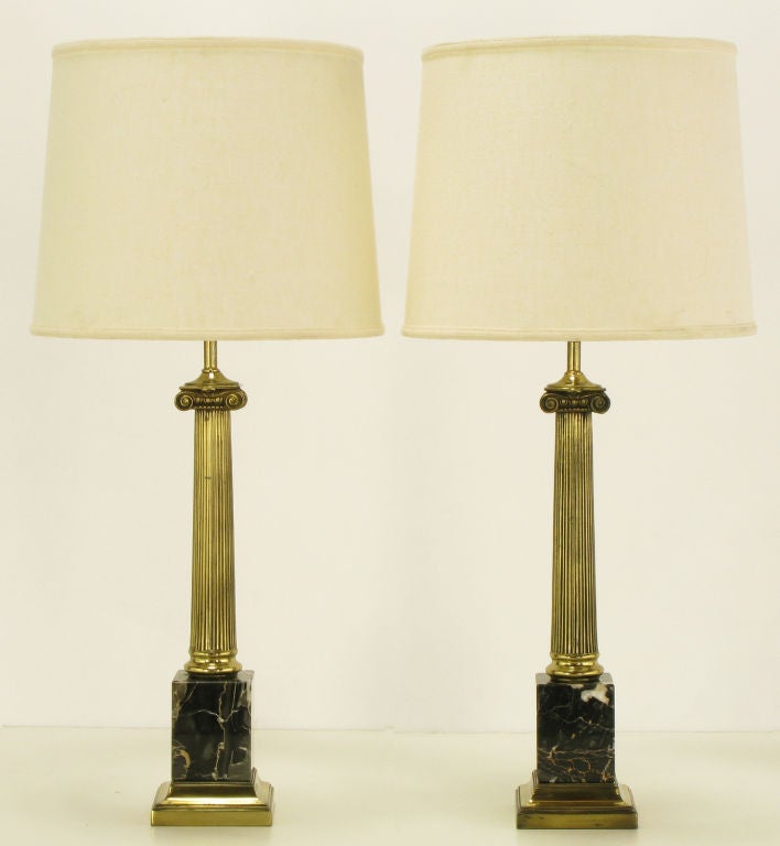 Pair of neoclassical ionic column table lamps with black Italian portoro marble block bases. Reeded brass columns with Greek style ionic capitals and stepped brass plinths. Brass socket and harp, sold sans shades. Possibly a Stiffel design.