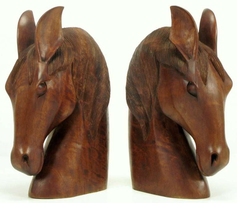 Carved from single pieces of wood, these striking horse heads possess an intriguing style. Certain features are exaggerated, in a somewhat Art Deco style. Measures: 22