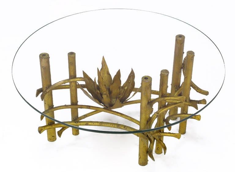 Petite coffee table, featuring heavy iron base supports and original glass top. Has a total of six legs, with sinuous iron stretchers that support the asymmetrical placement of a metal lotus flower. In the manner of Silas Seandel.