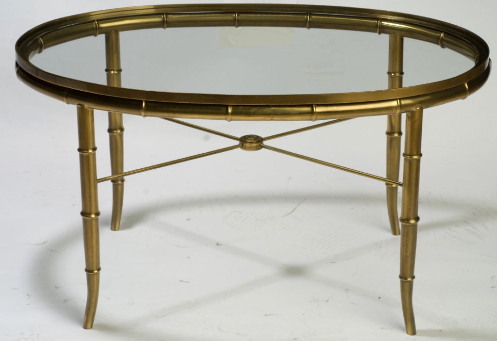 Versatile size oval table with splayed faux bamboo legs, cross stretchers with center medallion ornament. Glass top recessed into vertical brass frame that creates an solid integral gallery rail.