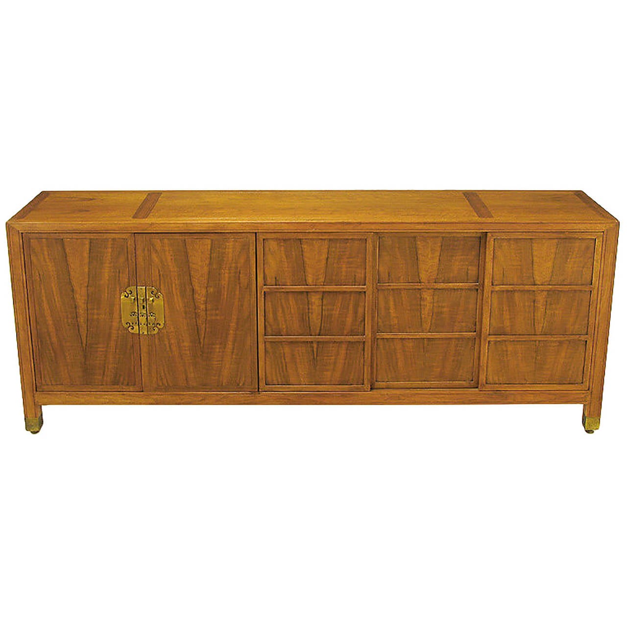 Baker Far East collection figured walnut sideboard. Pair of hinged doors with large solid brass escutcheons open to reveal four drawers. Set of three siding doors with recessed panels move side to side to reveal an open single shelf compartment.
