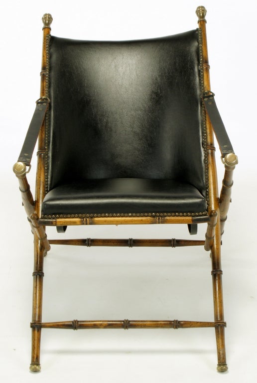 A Classic design, with folding wood frame carved to appear as bamboo, brass caps, leather seat and back with brass nailhead trim, and leather arm straps.