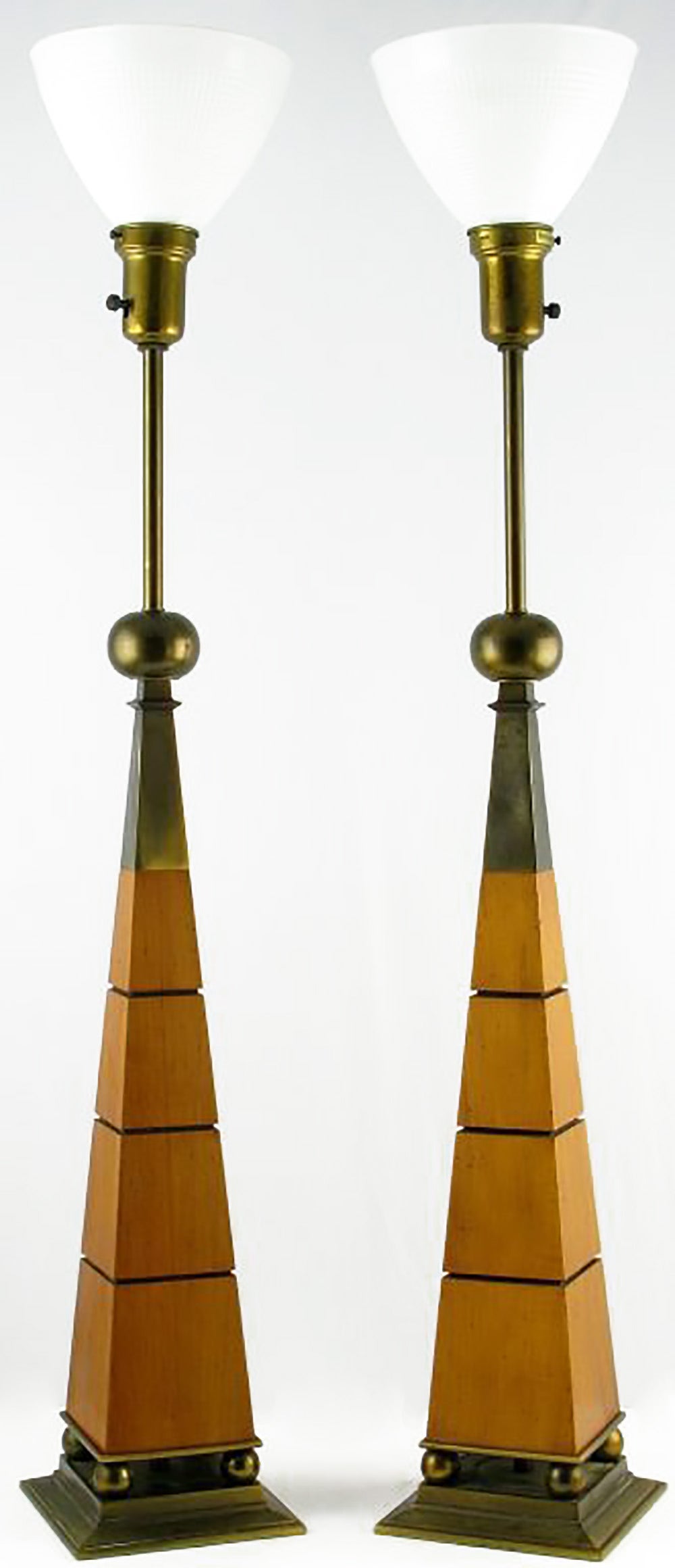 Architecturally inspired pair of table lamps by Stiffel. Four brass spheres atop a plinth base support a walnut obelisk-form body with horizontal incised and ebonized decoration. Surmounting the wood is a brass obelisk topped by a larger brass