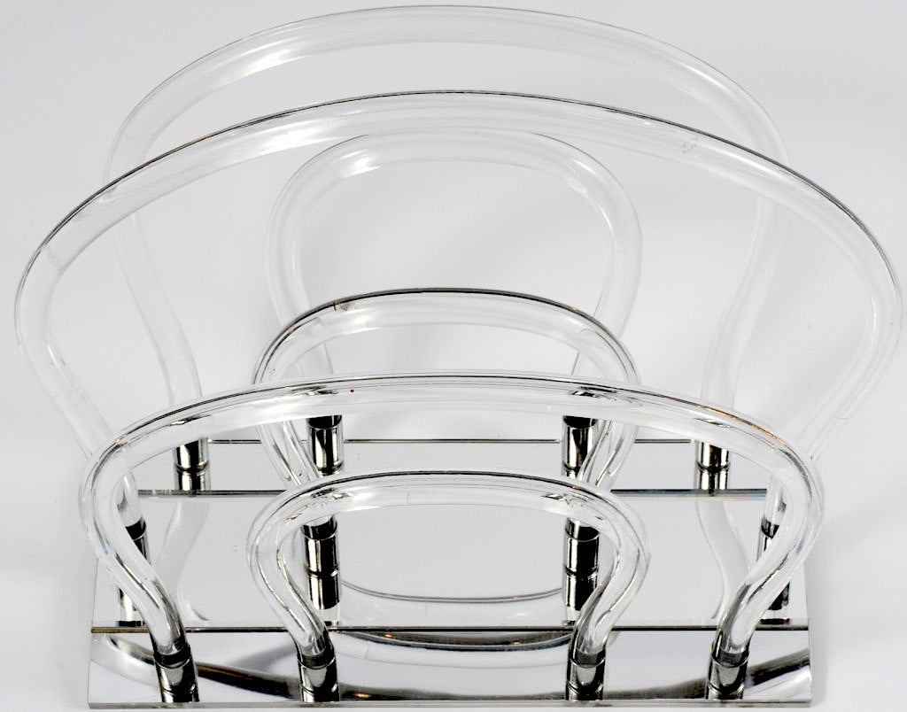 In the manner of Dorothy Thorpe, this sculptural magazine rack has a mirrored base that holds twelve chrome sockets into which the Lucite uprights are secured.