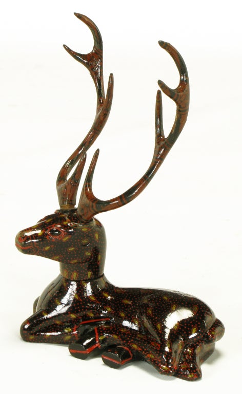 Hand carved wood recumbent deer with large horns and articulated head. Hand painted in a black lacquer with red dots and gilt tear drops outlined in red. Horns are hand painted in a native american style.