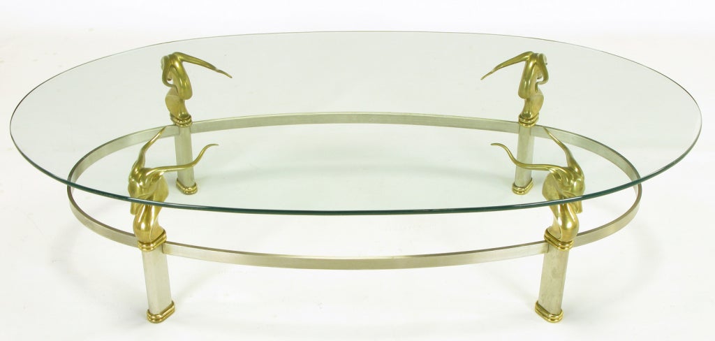 Art Deco revival oval form coffee table constructed of brushed stainless oval stretcher and canted legs. Brass gazelle heads with double oval brass beading at the legs. Glass top is 3/8