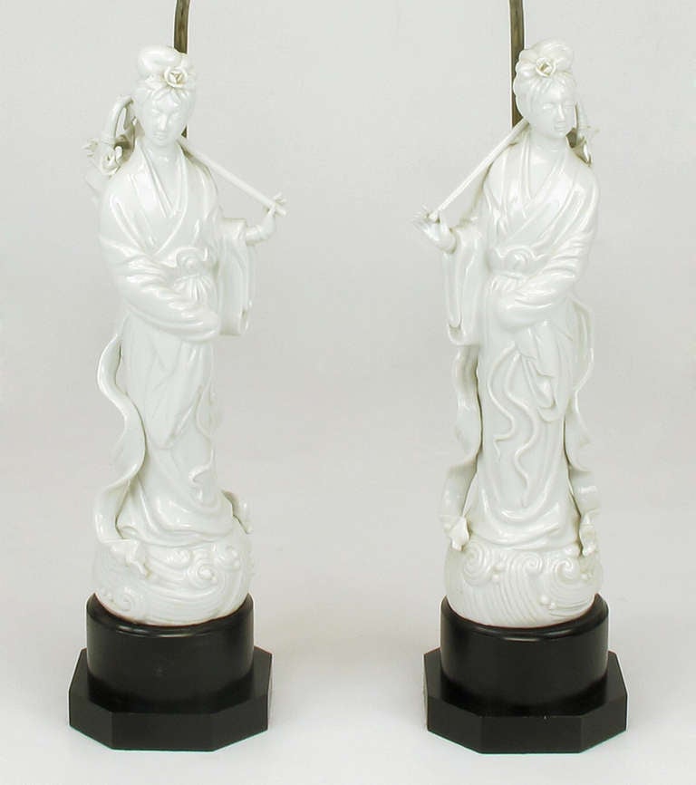 Pair of white porcelain blanc de chine table lamps. Asian statuettes of women carrying baskets of roses over their shoulders. Black lacquered wood base with octagonal plinth. Brass stem and socket. Sold sans shades.  

Statues are 17