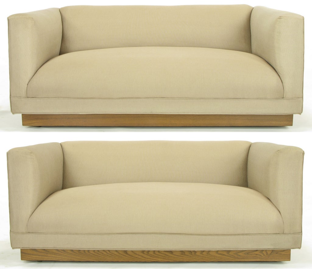 Uncommon even arm settees or loveseats with oak plinth base. Squared outside arms and back with curvaceous inner arms, tight seat and tight back. Original silk blend fine stripe tactile upholstery.  Purchased in late 1960s at Chicago's Merchandise