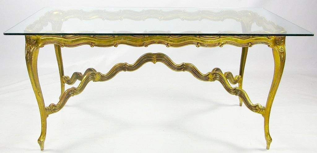 In a stylized Louis XV design, this table is a mid-century interpretation of a traditional form. The cast and gilt aluminum frame is strong for its svelte profile, so it is visually lighter than its wood counterparts, with the clear glass top adding