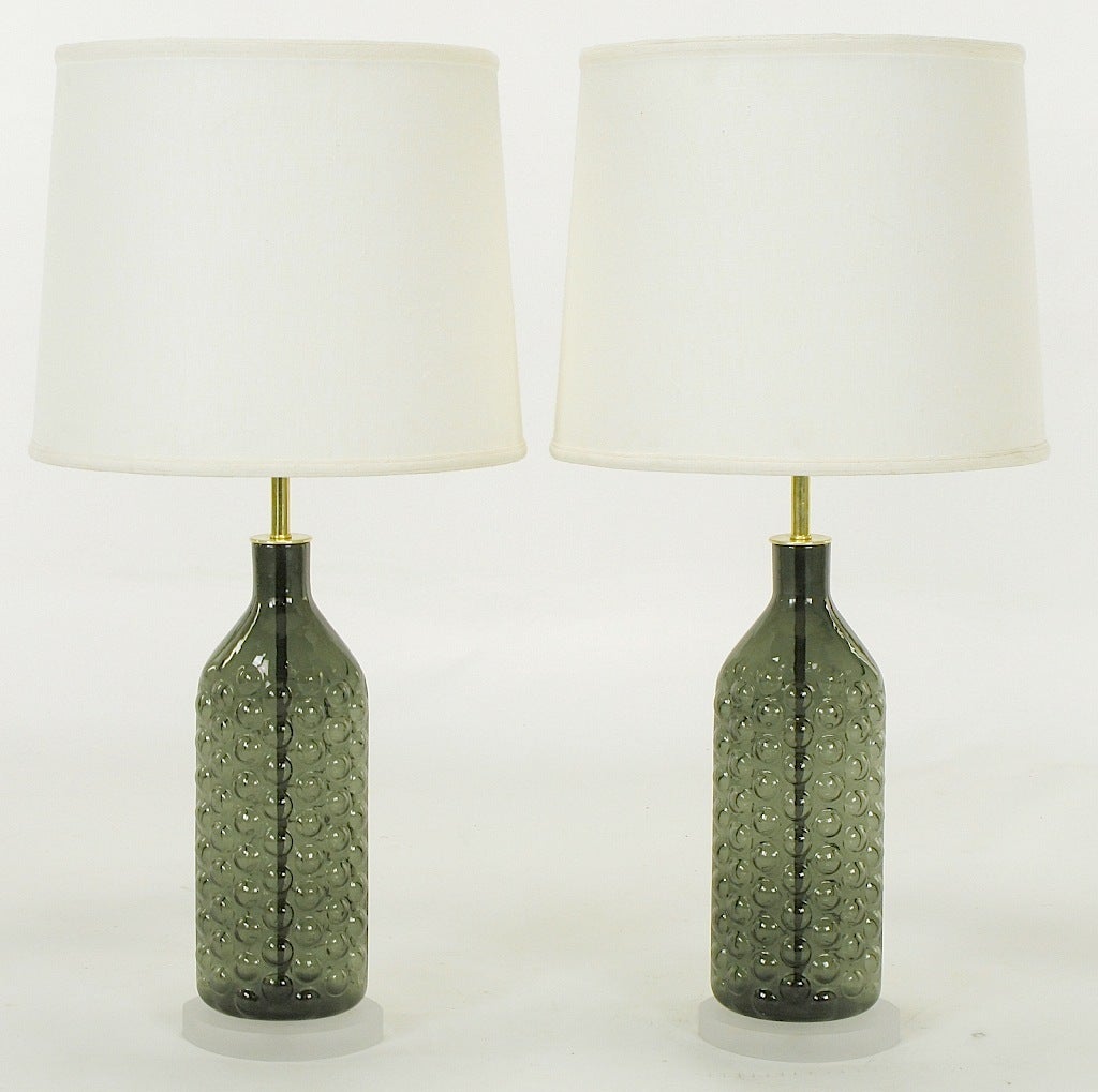 Pair of Blenko hand blown elliptical bubble glass bottle vases fashioned into elegant table lamps. The glass vases are mounted to elliptical frosted Lucite bases that echo the shape of the bottles. Brass stem and double cluster socket with brass