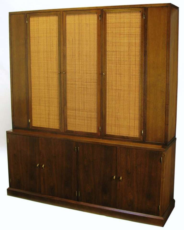 From a home with Widdicomb and Harvey Probber pieces, this is a fine quality custom made walnut two-piece cabinet, with removable top. Three woven cane covered doors open to reveal a shelved section. Bottom section features two drawers and