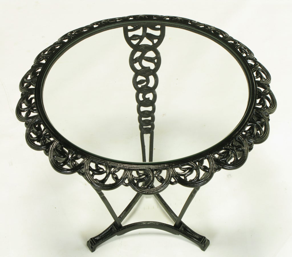Intricately cast iron side table with scalloped sloped apron and glass top. Tripodal leg formation with a triangular base. Each leg is comprised of interconnected descending circles with foliate details.  Possibly English in origin.