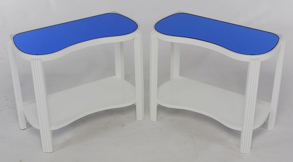 Uncommon pair of American art deco end tables finished in white gloss lacquer with blue tinted mirrored tops. Sinuous top and lower tier supported by reeded and canted legs.