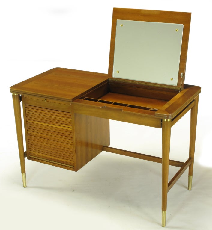 John Widdicomb bleached walnut flip top vanity with single floating tambour door side cabinet. Flip top opens to reveal a mirror, open compartment and segmented tray. Tambour door rolls up to reveal three drawers with top pull out surface. Tapered