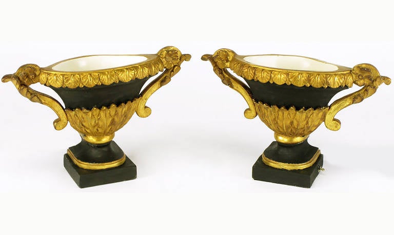 Cast plaster and gesso neoclassical or empire style double armed urn lamps in parcel gilt and black lacquer finish. The interior is fitted with a single socket for beautiful up light illumination. Acanthus leaf and scrolled arm detailing. Toggle