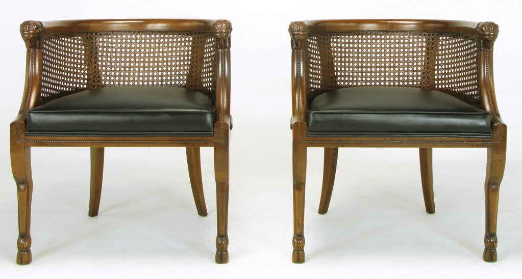 Empire style barrel back arm chairs. Each chair has a pair of hand carved ram's heads at the peak of the front legs which are dramatically shaped similar to actual ram hind legs with hooves as feet. New Spinneybeck black leather seats with caned