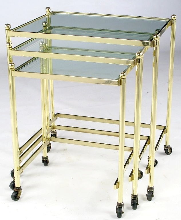 An extremely well-crafted set of three nesting tables in solid brass. The workmanship is on par with that of Maison Jansen. The brass ball finials add an elegant touch and the casters facilitate ease of movement. The clear glass is new, and a