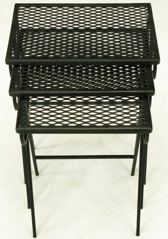 Classic set of three wrought iron nesting tables attributed to Maurizio Tempestini for Salterini. Inverted V shaped lags with double loops, lend to the appearance of bows. Iron mesh tops welded into L channel frame. Fresh black satin enamel.