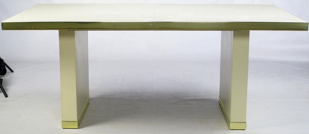 Dining table from Pierre Cardin, in ivory laminate and gold anodized aluminum banding at the top and base. Comes with 2 leaves that measure 18