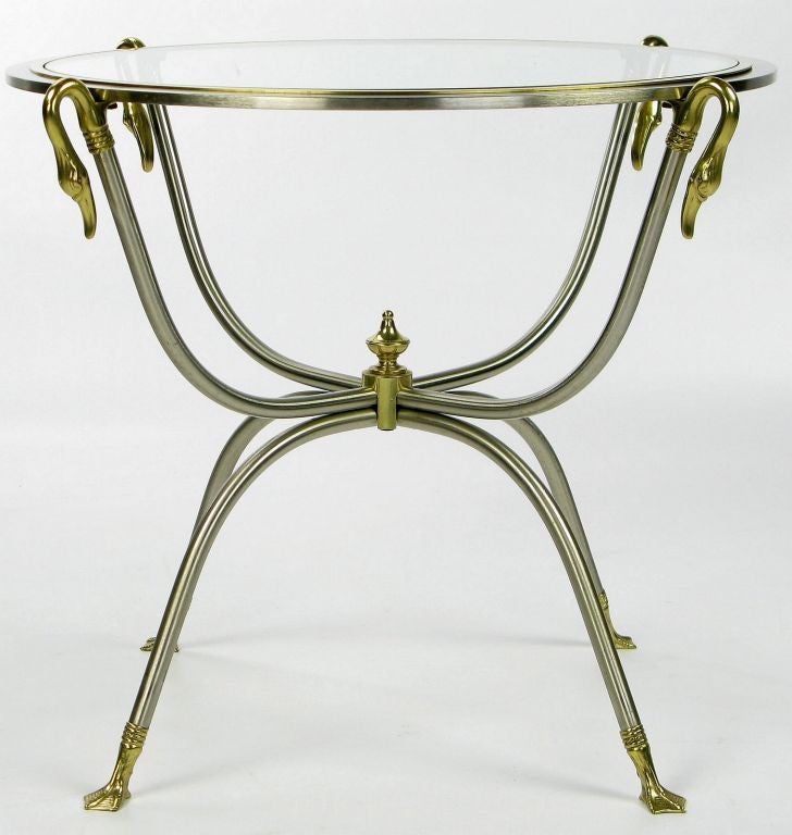 Jolie table d'appoint ronde avec un cadre à double curule en acier nickelé et laiton. Le plateau en verre transparent est entouré d'un cadre en nickel et en laiton, soutenu par quatre longs cols de cygne en laiton.