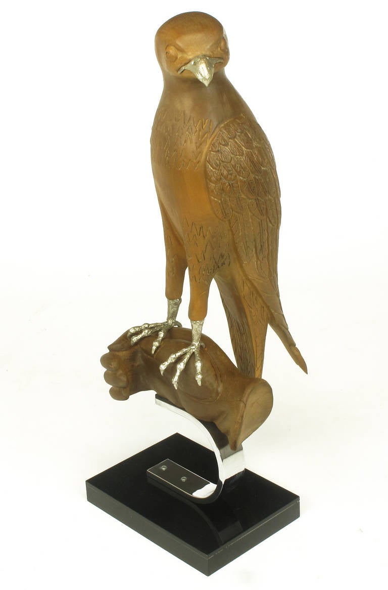 Wonderfully carved falcon or hawk, mounted on a carved wood hand. Silver talons and beak. All surmounted on a C-shaped chrome steel bracket and black acrylic over wood base.