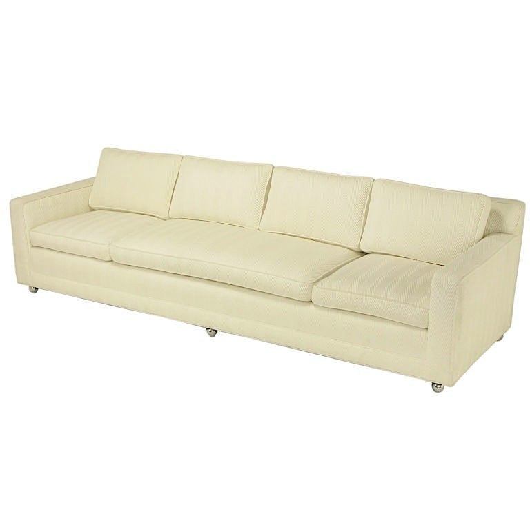 Eight and a half foot long loose cushion sofa, attributed to Baker. Upholstered in an elegant white herringbone backed cotton, with wide center seat cushion characteristic of Baker sofas of the time, with six chrome ball casters. Casters can be