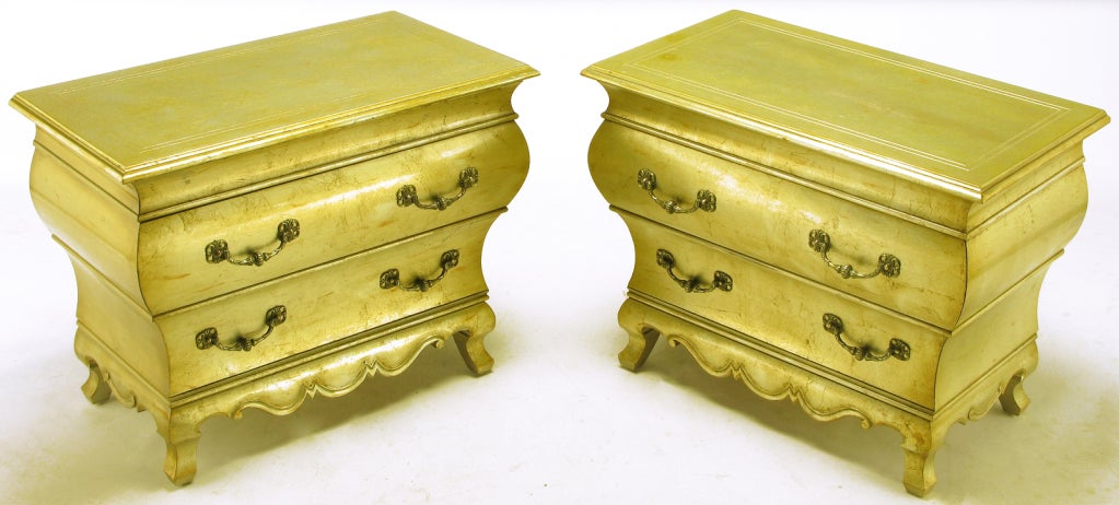 Possibly a Dorothy Draper design for Henredon, these bombe' two drawer commodes are finished in a distressed gold toned silver leaf with carved apron and legs. The U shaped drop pulls are solid cast brass. Variations in finish are intentional in