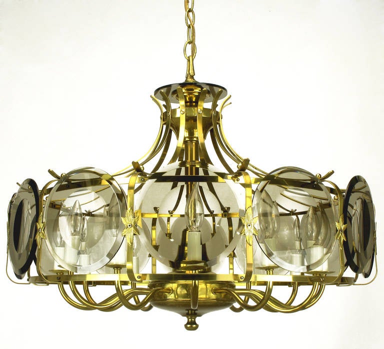 Uncommon brass chandelier with a ring that houses twelve smoked glass lenses and is suspended by twelve curved brass arms that meet and connect to the centre stem. Smoked Lucite disc accents the top. The brass ring encircles a twelve-arm chandelier