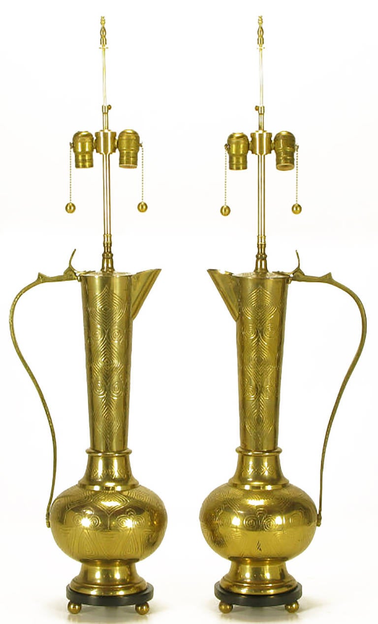Pair of cast and etched brass ewers, or carafes, converted to table lamps. Black lacquered wood base with brass ball feet. Brass stem and dual socket cluster with brass ball pull chain. Sold sans shades.
