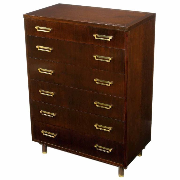 Beautiful wood grain and solid brass U-shaped drop pulls are the focal points of this elegant and clean lined tall chest by Baker Furniture. The base is comprised of four cylindrical legs with brass sabots and stretchers that run through the legs to