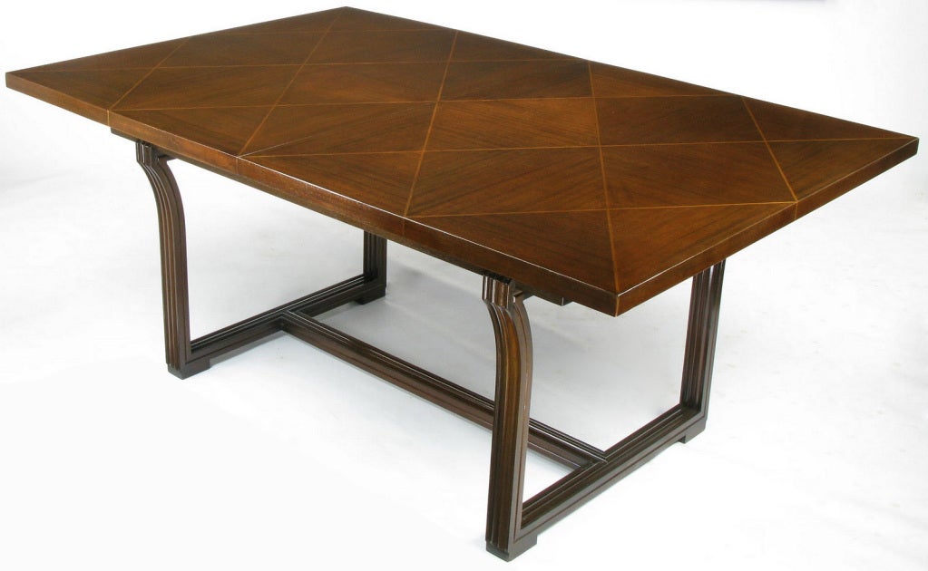 Rare example of a fine dining table by Tommi Parzinger for Charak Modern. Harlequin patterned parquetry inlaid top of ribbon mahogany and lighter wood surmounted on a rare, and most probably custom, carved mahogany sled base with low stretcher. The