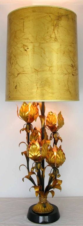 Large and striking gilt metal table lamp with illuminated foliate details. Four lotus flowers each contain a socket for candelabra base light bulbs. The metal base is finished in black lacquer. Sold sans shade.