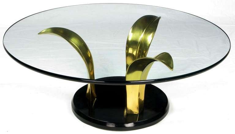 A striking round cocktail table reminiscent of organic design. The base is comprised of three large brass palm leaves and a lacquered wood disc with beveled edges. The glass top is considerable at 1/2