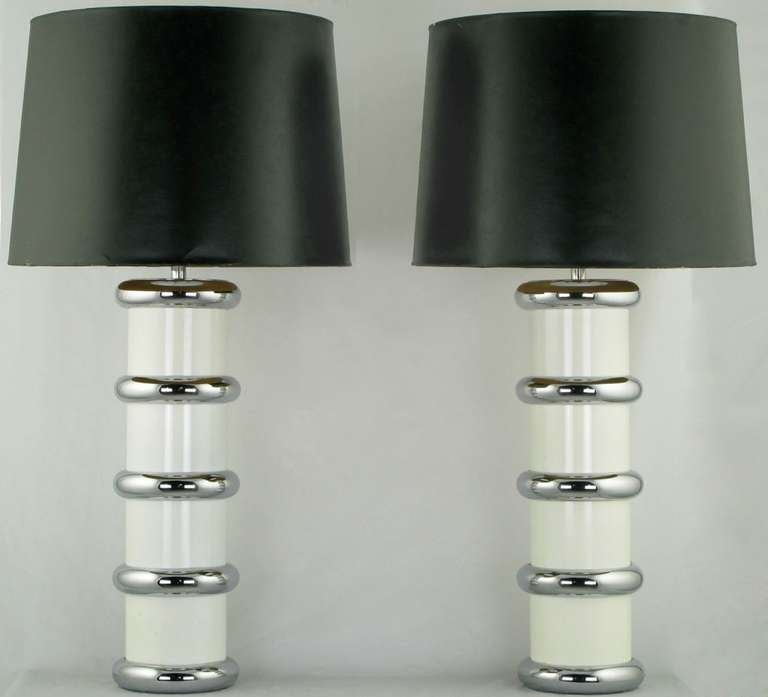 Pair of tubular form table lamps in white enameled steel with chromed steel cuff rings, stem, socket and harp. From the Mutual Sunset Lamp Company; a now defunct lamp company that featured designs by Gilbert Rhode, among others. Sold sans shades.