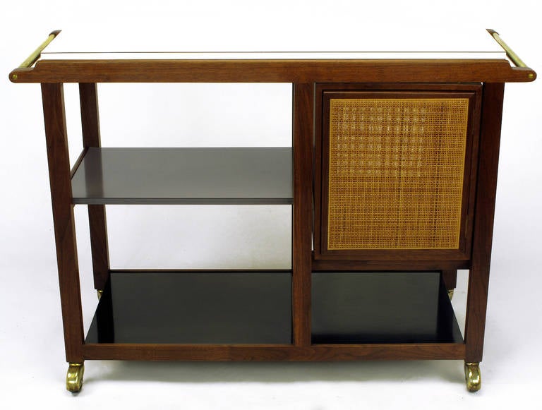 A rarely offered dual-sided bar cart or server by Edward Wormley for Dunbar. The frame and cane front cabinet are comprised of walnut wood and the service areas are a combination of black, slate gray and white micarta. The casters and handles are