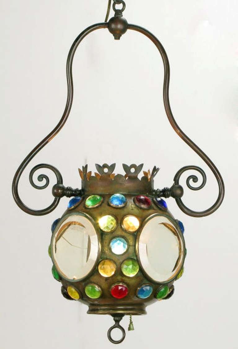 Spherical brass light fixture, with open bottom and top, and four flat sides with clear beveled glass inserts. Inset into the brass shell are faceted glass pieces in yellow, blue, green and red. Crenelated pierced brass crown. Appears to have