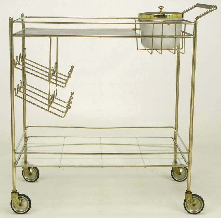 Brass bar cart with two inset glass surfaces and casters. Comes with original cast resin ice bucket, and tilted, eight-bottle holder. Cross hatch brass wire glass surface supports and brass wire wrapped handle add dimension and visual appeal.