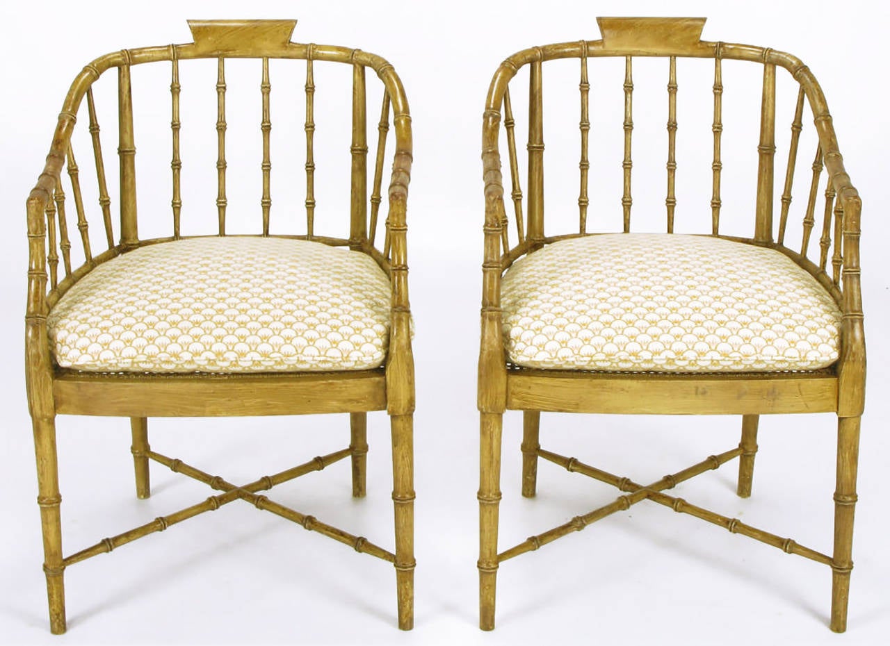 Pair of carved wood bamboo-form arm chairs with an antiqued nutmeg toned glaze. X-stretcher leg supports with woven cane seats and silk blend upholstered loose cushions.