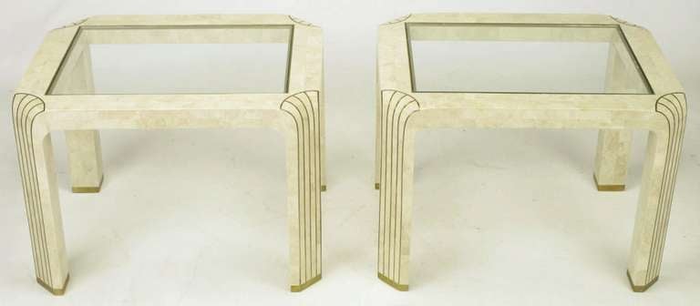 Pair of tessellated fossil stone and inlaid brass side tables. Glass tops bordered by brass trim. Canted corner legs feature brass inlaid elongated shell motif and brass sabots. Manufactured in the Philippines, as were the tessellated stone