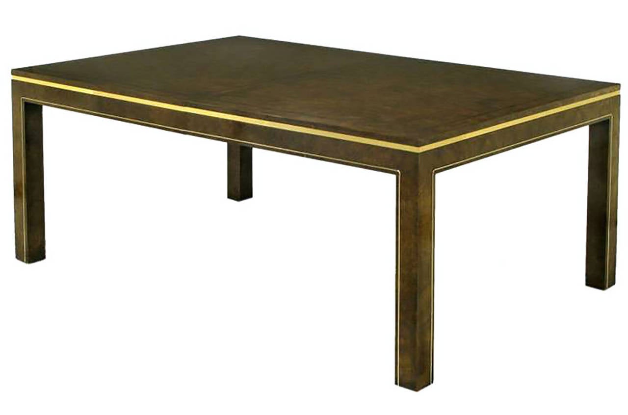 Clean lined parsons style dining table in an exquisite burl amboyna wood, with rosewood inlaid top border, from Mastercraft. Brass banding just below the top and brass welting details to the legs and skirt. Comes with two leaves; making the over-all