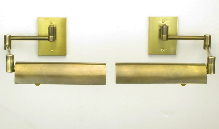 Rare pair of pharmacy swing arm sconces constructed of solid brass with a brushed finish to the shade and back plate. Bakelite umber knobs and three way sockets with fresh ivory lacquer inside coating. Rewired and lightly refinished with out taking
