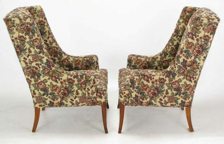 Pair of circa 1940's low arm wing chairs upholstered in a fruit and foliage tapestry. Mahogany saber legs have a lightly carved detail. In a similar style to early Grosfeld House with low turned arms and  exaggerated rake to the chair back.