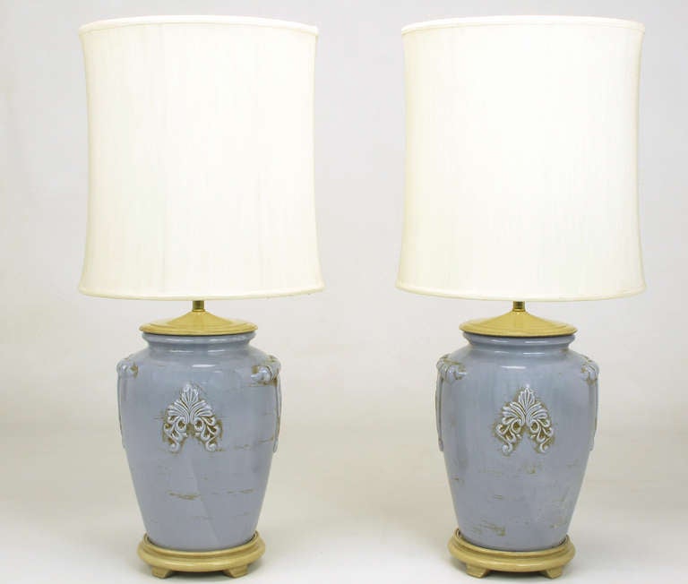 Pair of periwinkle blue ceramic vase or urn form table lamps with antique glaze. Cap and base are carved and lacquered wood with a bone glaze, brass stem and double socket cluster. Sold sans shades.