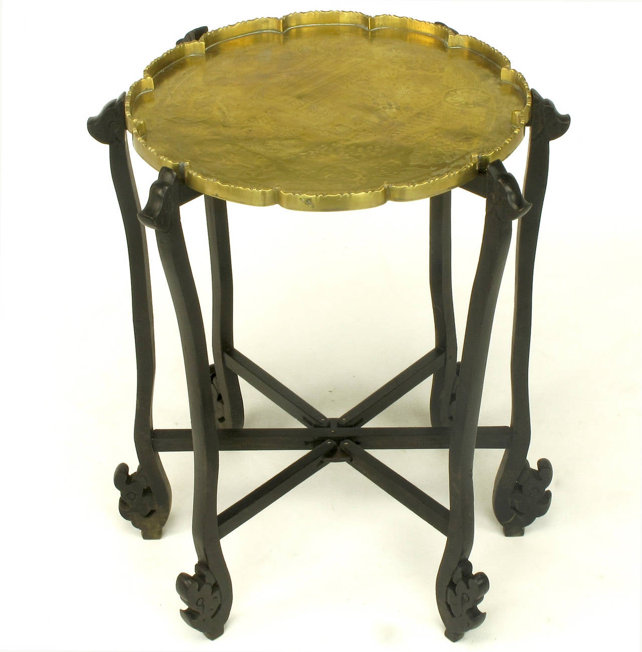 Exotic folding tray table of carved ebony wood with six legs that fold flat. Etched scene into thick brass tray with scalloped edging can be seen in image 4.