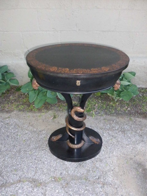 A quality 19th century style 1940's ebonized and gilt sewing table/stand with a fitted light wood interior, a stenciled frieze on top, carved eagles heads and paw feet on the base as well as a carved wood snake around the base shaft. A nice looking