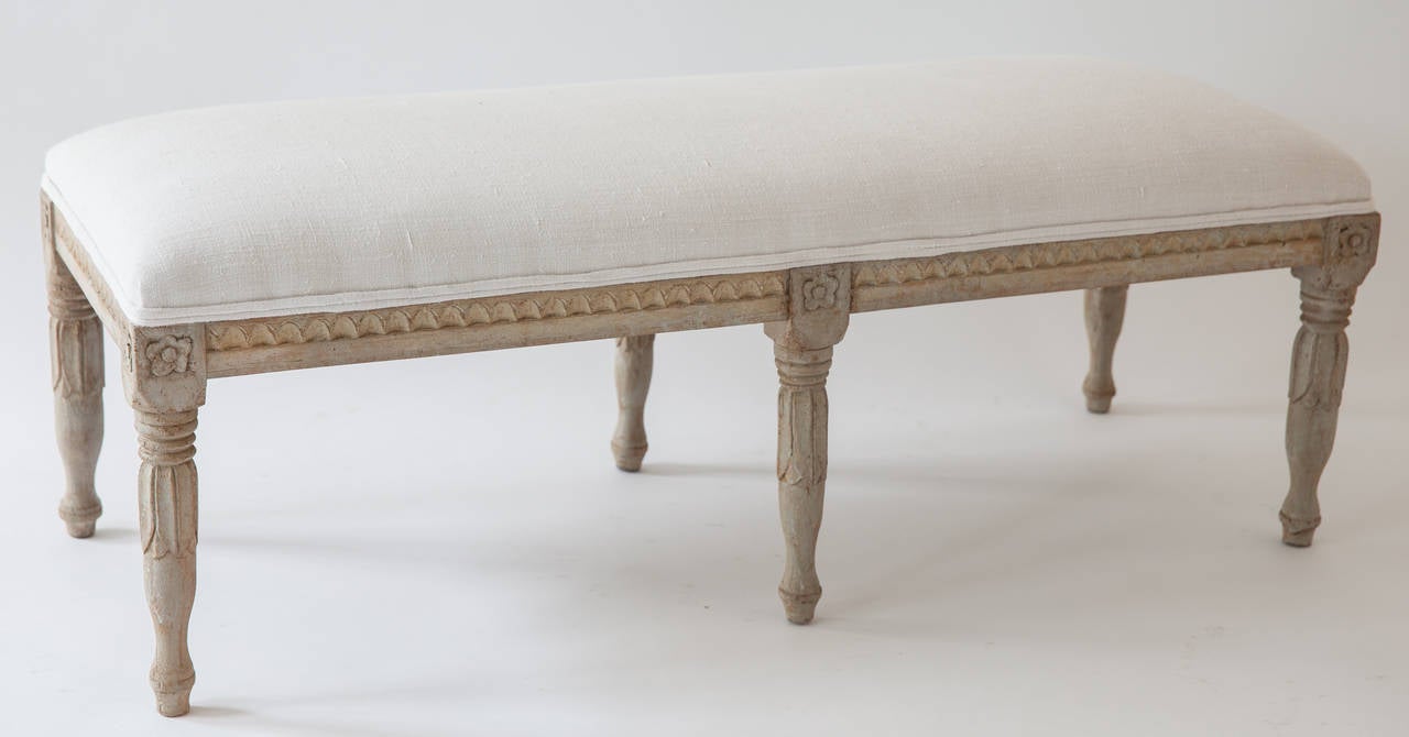 A Swedish Gustavian style bench with beautiful carved details in the Gustavian manner, circa 1880. This bench is the perfect size to fit at the foot of a bed or under a window. The old paint surface is excellent, it has been reupholstered in a