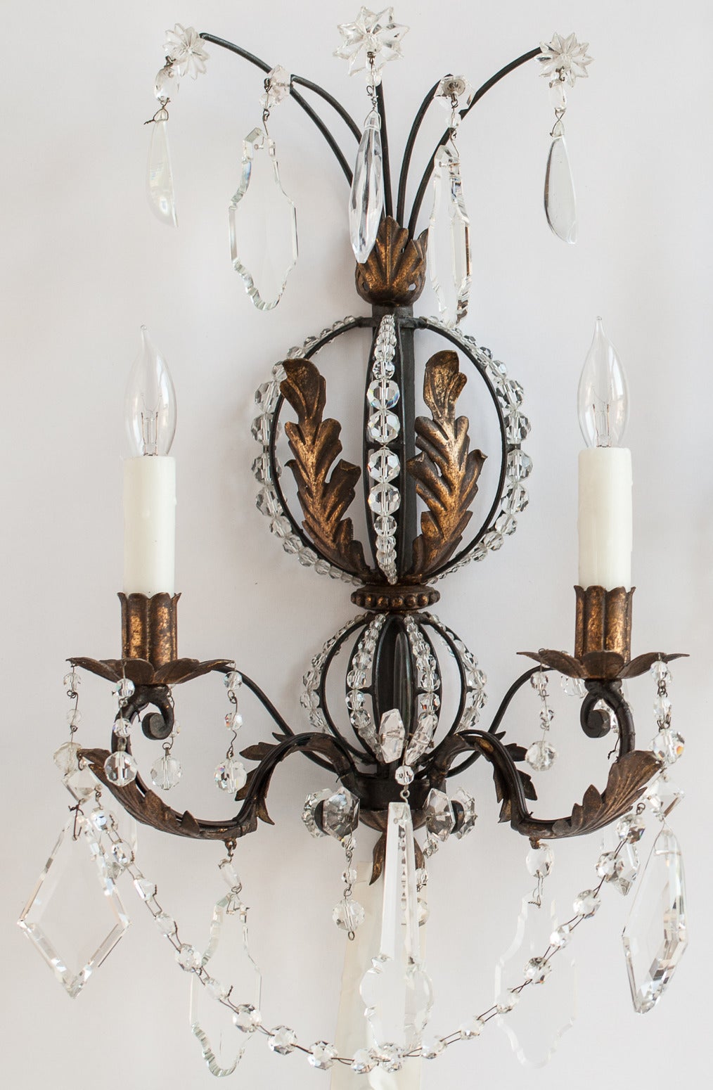 A glamorous pair of French gilt leaf and crystal sconces with two lights and beeswax holders. The sconces have two graduated circles of crystal beads and leaves in the center ending with two lights and a series of large crystals at the bottom. At